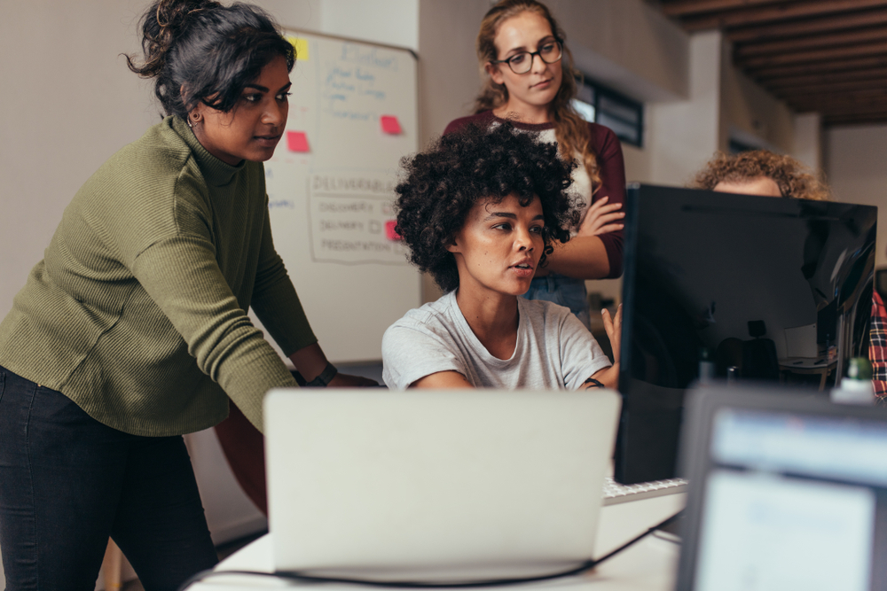 A group of people standing at computer and laptop